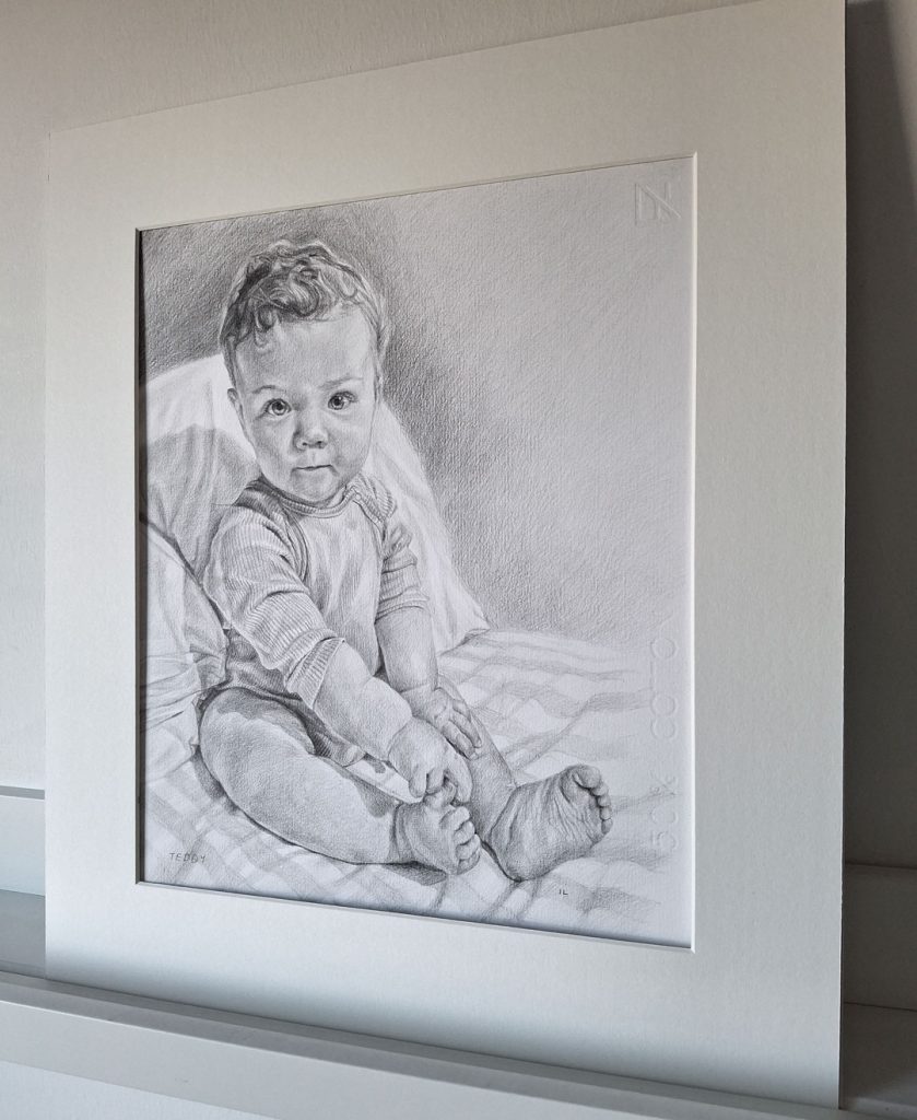 mounted pencil sketch of a baby boy sitting on a bed