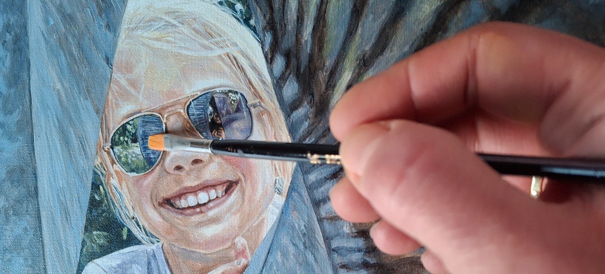 detail of an artist hand painting a portrait of a girl in sunglasses