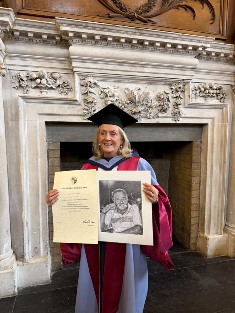 smiling lady holding a pencil portrait of her brother during her graduation celebration